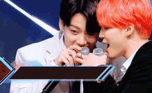 a man with red hair is holding a microphone while another man looks on