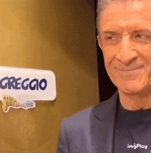a man in a suit is smiling in front of a sign that says greggio