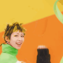a woman wearing a green and orange jacket is smiling with her arm in the air