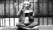 a person wearing a mask is sitting on the ground reading a book and drinking from a cup .