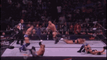 a group of wrestlers are wrestling in a ring with a referee .