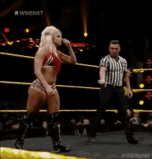 a female wrestler is standing in a wrestling ring with a referee .