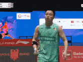 a man wearing a green petronas shirt stands in front of a red wall