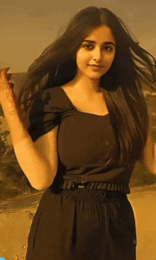 a woman in a black dress is standing in the sand with her hair blowing in the wind
