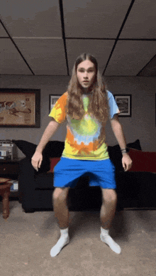 a man in a tie dye shirt and blue shorts is jumping in the air