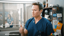 a man in a blue scrub is giving a thumbs up in front of a nbc logo