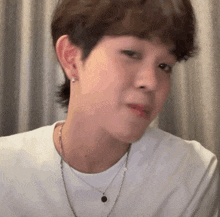 a young man wearing a white shirt and a necklace