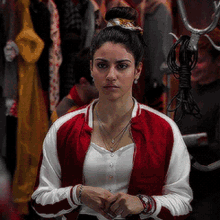 a woman wearing a red and white jacket is standing in front of a bunch of clothes