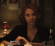 a woman with red hair is sitting at a table with a lamp