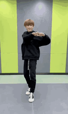 a man wearing a black sweatshirt and black pants is standing in front of a yellow and grey wall