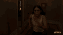 a woman in a white tank top is running in a dark room with netflix written on the bottom