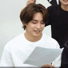 a man in a white t-shirt is holding a piece of paper in his hand .