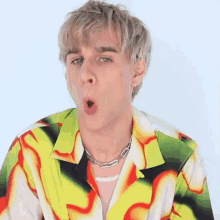 a young man wearing a colorful shirt and a chain around his neck makes a surprised face