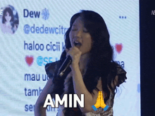 a woman singing into a microphone with the word amin on the bottom right