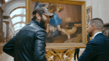 two men are looking at a painting in a museum and one of them is wearing a hat that says ' ny ' on it