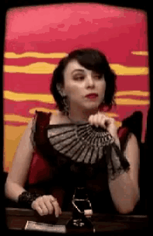 a woman in a black dress is holding a fan in front of a red and yellow background
