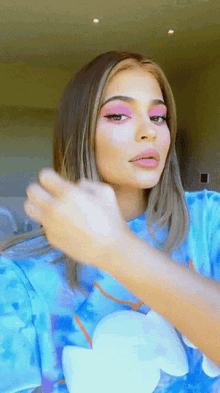 a woman wearing a blue tie dye shirt has pink eye shadow on her face