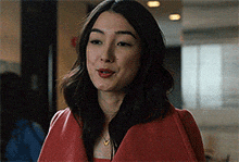 a woman is wearing a red coat and necklace