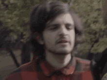a man in a plaid shirt says ok in front of trees
