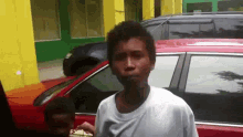 a man in a white shirt is standing in front of a red car and a yellow building