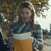 a woman in a colorful sweater is holding a piece of paper