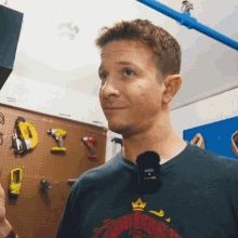 a man wearing a rode microphone stands in front of a wall full of tools