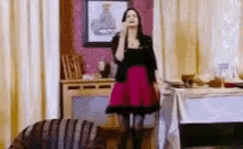 a woman in a pink skirt is dancing in a living room while talking on a cell phone .
