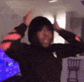 a man in a black hoodie is standing in a room with his hands in the air .