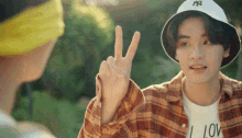 a young man wearing a hat and a plaid shirt is giving the peace sign .
