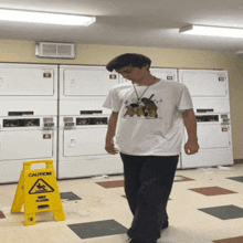 a man walking in a laundromat next to a caution sign