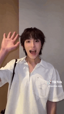 a young man wearing a white shirt is waving his hand .
