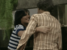 a man in a plaid shirt is hugging a woman