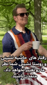 a man wearing sunglasses is holding a cup of coffee in a park