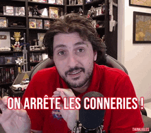 a man in a red shirt is sitting in front of a microphone and says " on arrete les conneries "