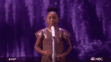 a young girl singing into a microphone on a stage with the nbc logo in the corner