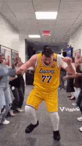 a man in a lakers jersey is dancing in a hallway surrounded by people