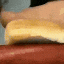 a close up of a person cutting a piece of cheese on a hot dog
