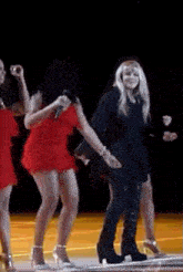 a group of women are dancing on a stage and one of them is wearing a red dress