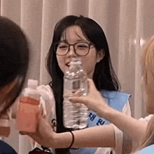 a girl wearing glasses is holding a bottle of water in her mouth .