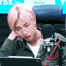 a man wearing glasses is sitting in front of a microphone in front of a sign that says tbs korea