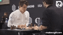 two men are playing a game of chess with a make a gif.com advertisement in the background