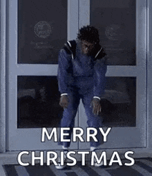 a man is standing in front of a door with his hands on his knees and says merry christmas .