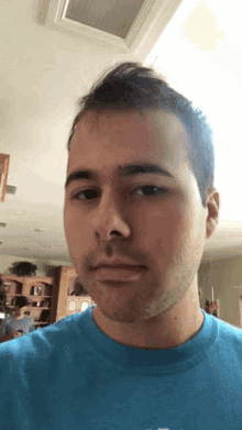 a man in a blue shirt looks at the camera with a serious look on his face