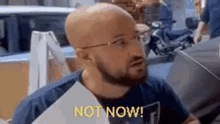 a bald man with a beard and glasses is holding a piece of paper that says `` not now '' .
