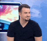a man with a beard wearing a black shirt is sitting in front of a television screen .
