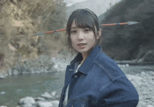 a girl with a spear on her head standing next to a river