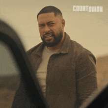 a man with a beard is standing in front of a car with the word countdown on the bottom right