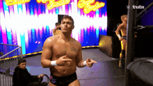 a shirtless wrestler stands in front of a sign that says ' wwe ' on it