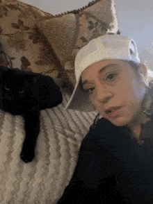 a woman wearing a white hat and a black cat laying on a bed