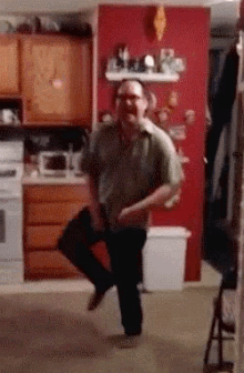 a man is dancing in a kitchen with a red wall in the background